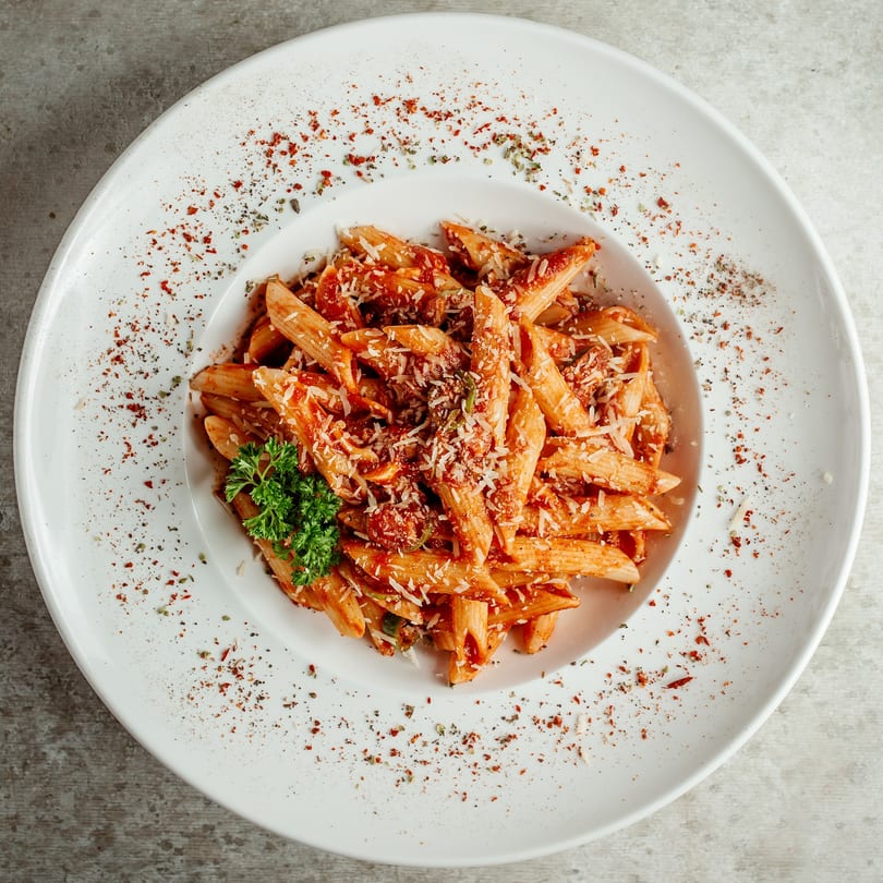 Penne pasta with red sauce, grated cheese, and parsley on a white plate with spices.