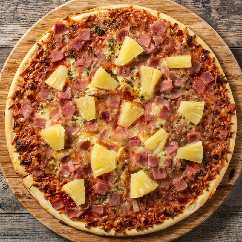A Hawaiian pizza with ham and pineapple on a wooden serving board, from Alberona's Davinci Pizza & Pasta.