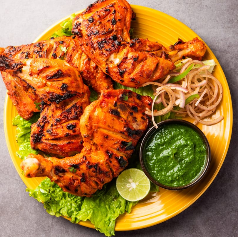 Grilled chicken pieces with charred skin, green sauce, sliced onions, and lime on a yellow plate.